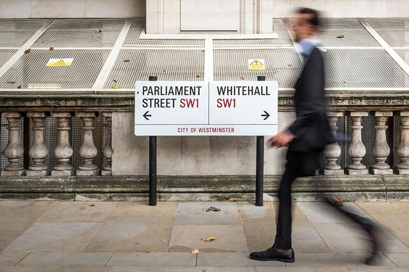 Street sign showing Parliament Street and Whitehall with a man walking past who is blurry